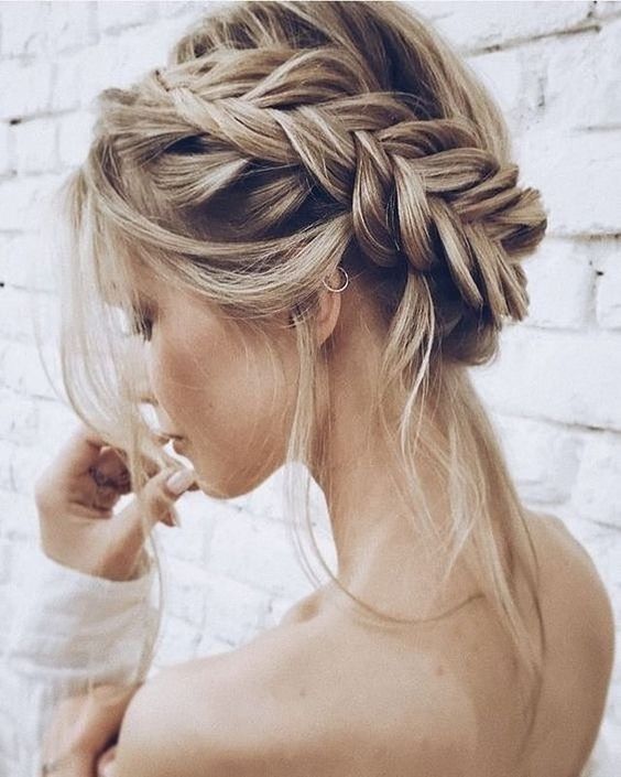 a braided messy low updo with a flower tucked inside and some little curls