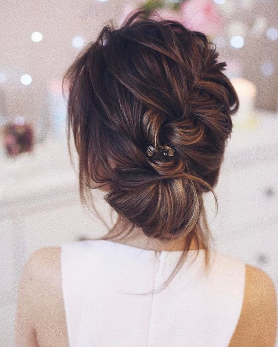 a casual braided and twisted low updo with bangs with some greenery in it