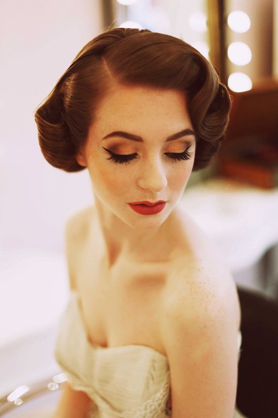 a vintage low updo with a twisted and wavy lower part and a volume on top plus a small hairpiece