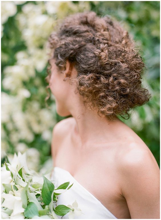 a curly low updo with locks down and twists with a single floral hairpin will add romance to your look